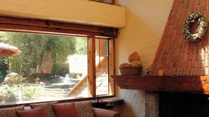 A cozy living room with a fireplace, a sofa, and a large window overlooking a garden. - Country House In The Woods With River (Valle de Bravo)