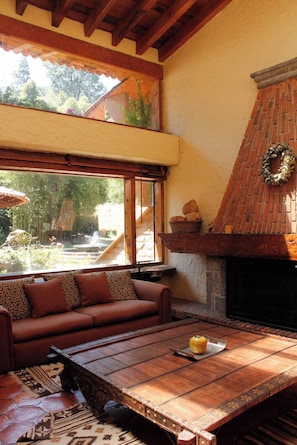 Uma sala de estar acolhedora com lareira, um sofá e uma grande janela com vista para um jardim.