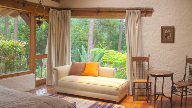 A room with a sofa, two chairs, a small table, and a large window with curtains. - Country House In The Woods With River (Valle de Bravo)