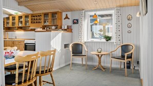 Une cuisine chaleureuse avec des meubles en bois, un coin repas avec des chaises en bois et une fenêtre agrémentée de rideaux.