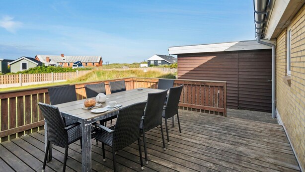 Une terrasse en bois avec une table et des chaises, donnant sur une pelouse, avec des maisons en arrière-plan.