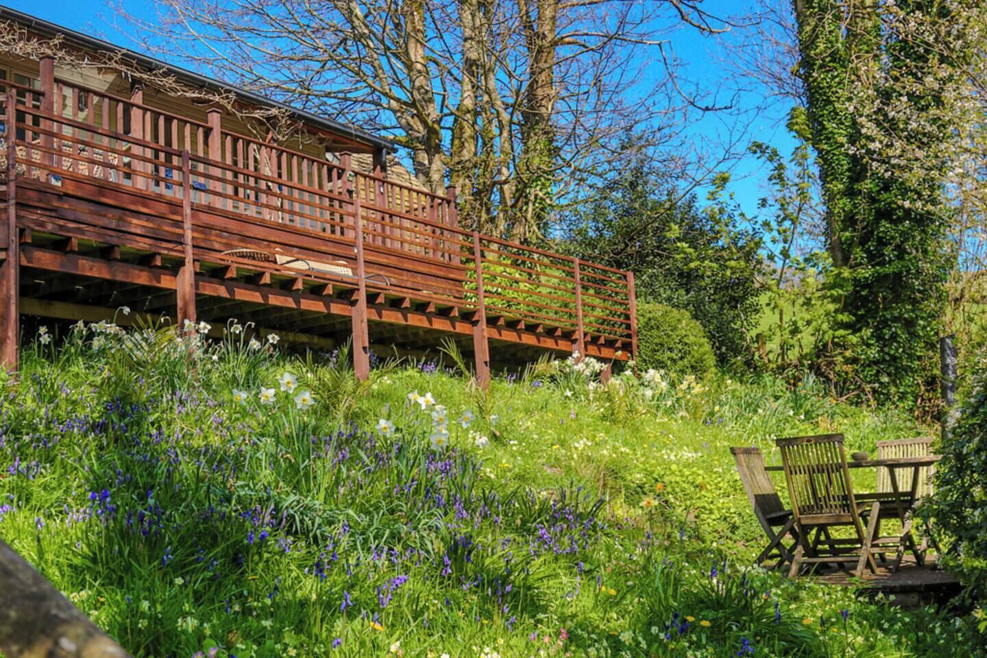 A wooden deck with a railing, surrounded by lush greenery and wildflowers.