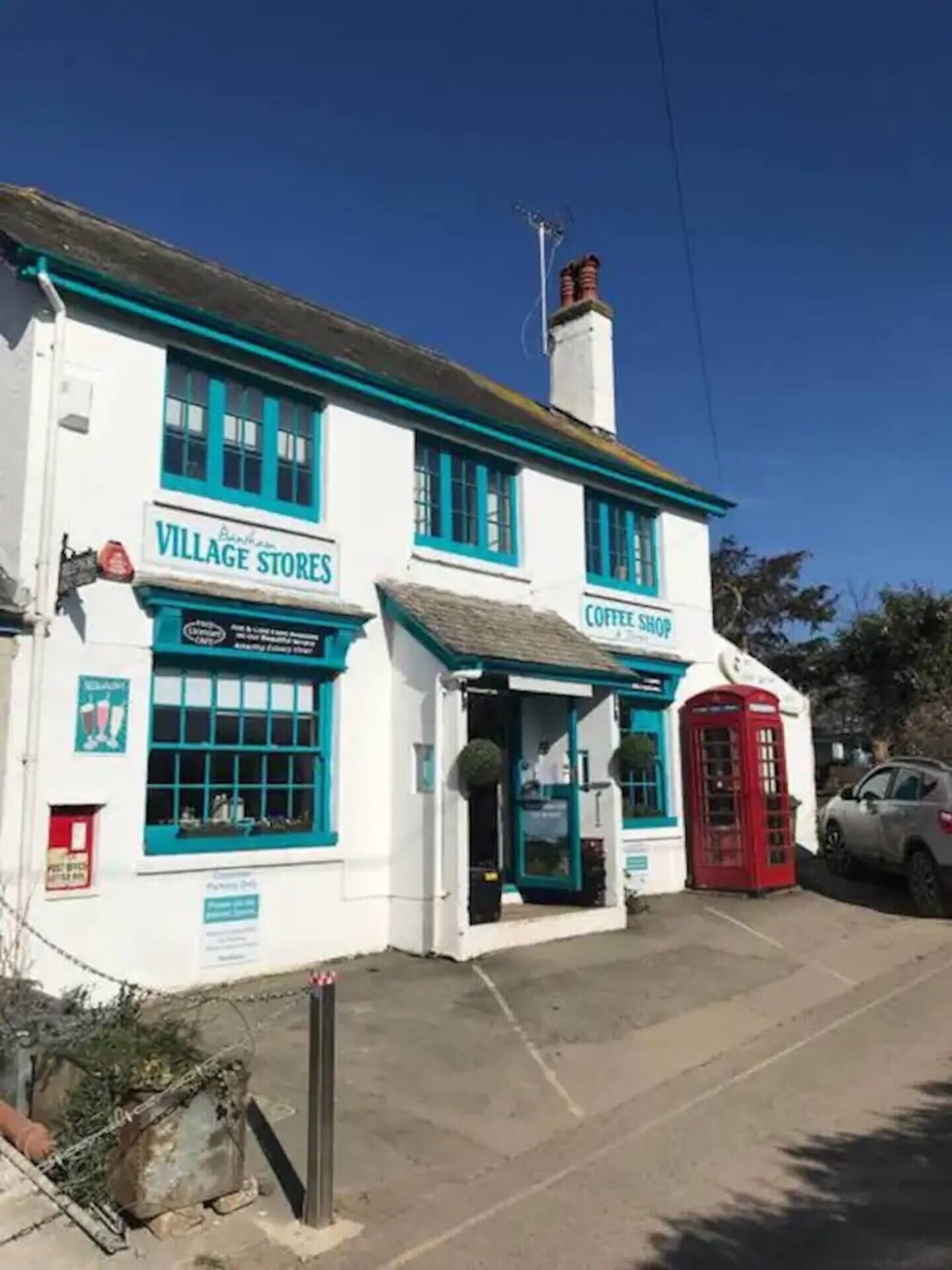 A white building with blue trim and a red telephone booth. It has signs for 'Village Stores' and 'Coffee Shop.'