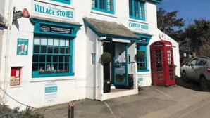 A white building with blue trim and a red telephone booth. There are signs for 'Village Stores' and 'Coffee Shop' on the building. - Treetops, a relaxing haven in Bantham South Devon (Bantham)