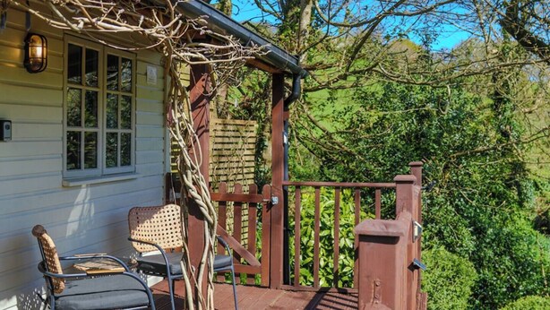 A wooden deck with a railing, a chair, and a table. - Treetops, a relaxing haven in Bantham South Devon (Bantham)