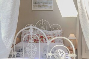 A bed with a white metal frame, floral bedding, and a wall-mounted picture.