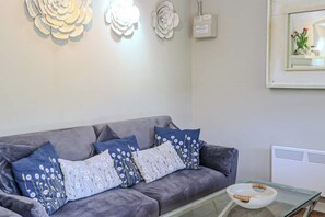 A living room with a grey sofa, patterned cushions, a glass coffee table, and wall-mounted decor.