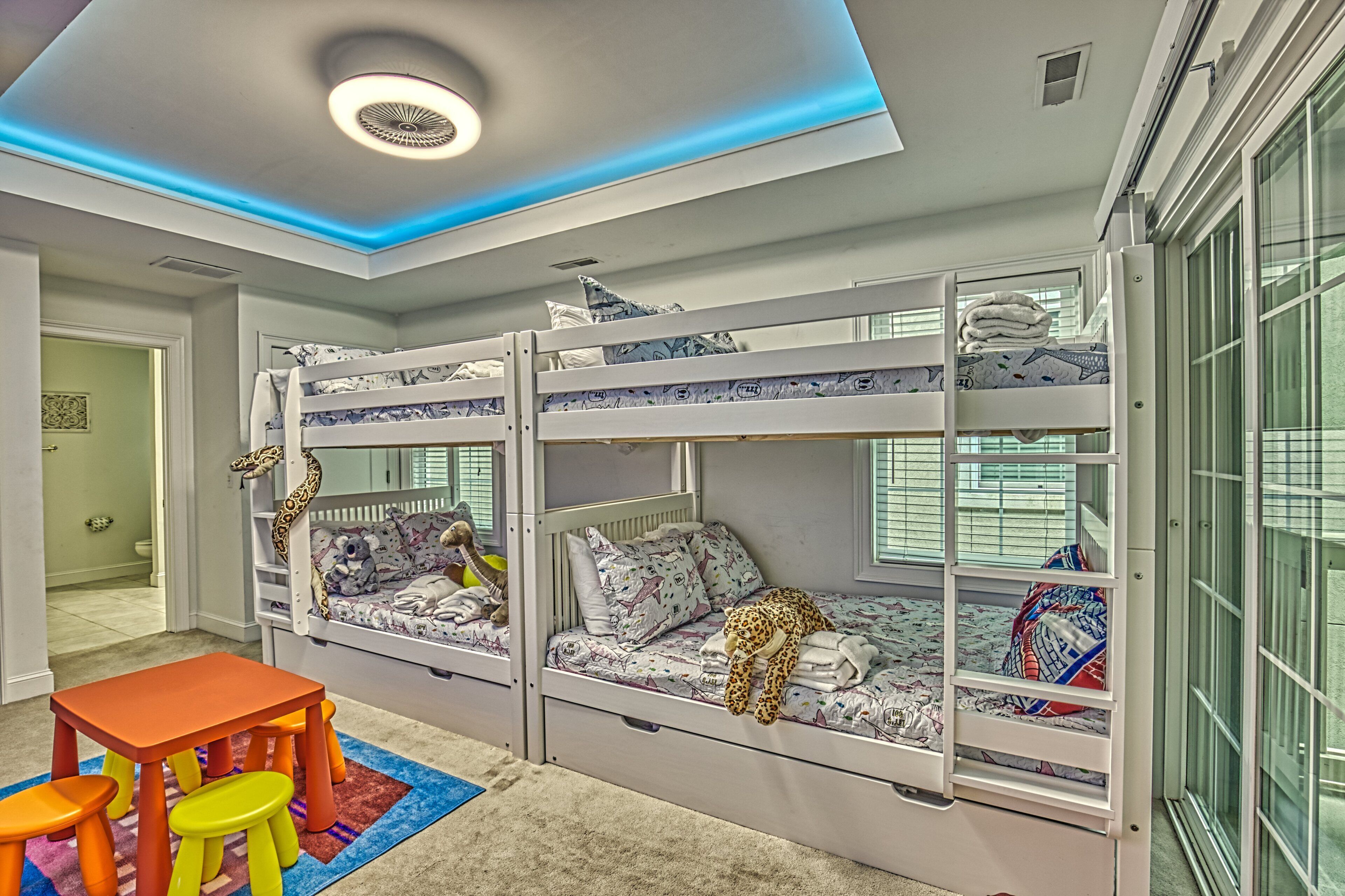 A children's room with bunk beds, a small table, and colorful stools.