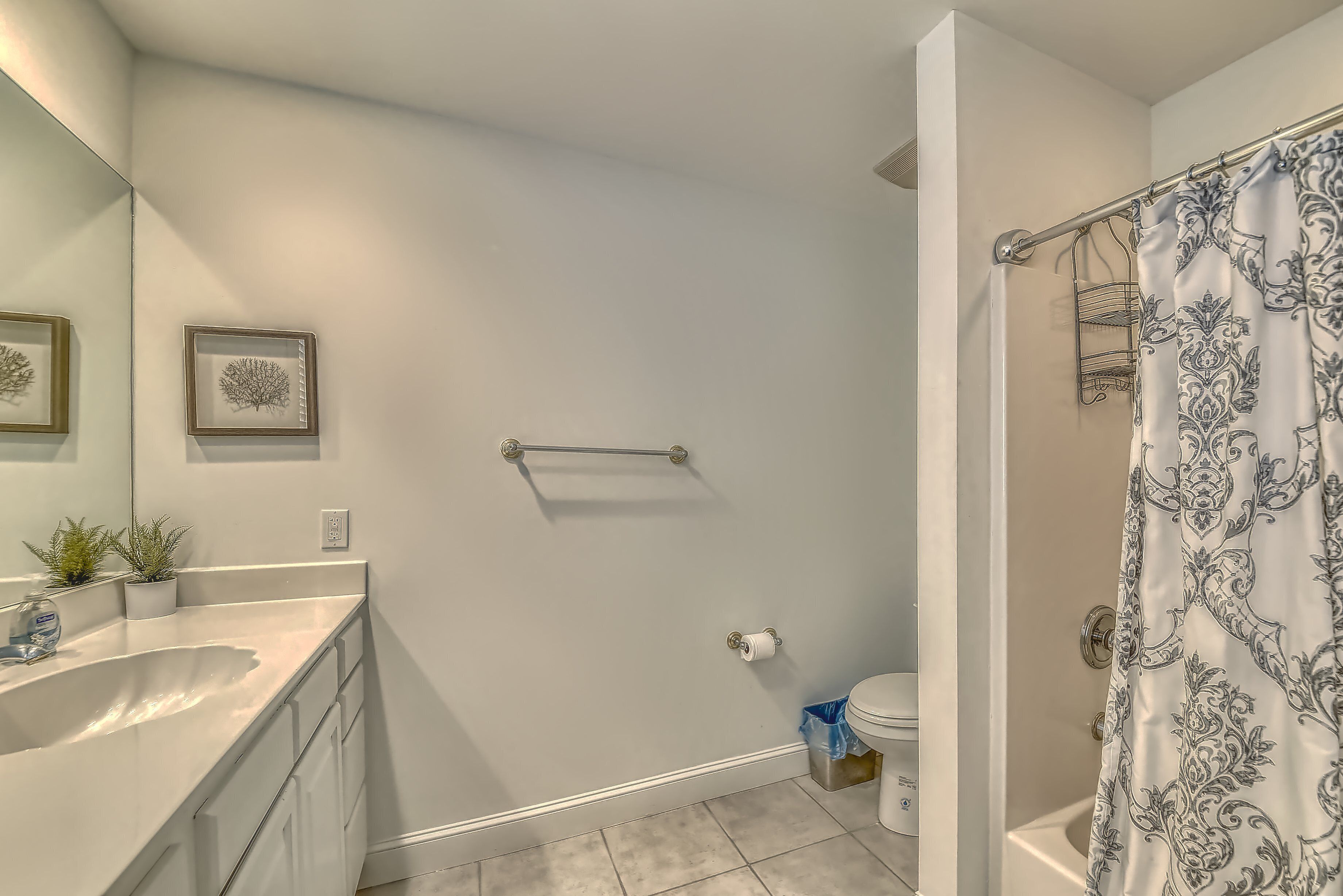 A bathroom with a white sink, mirror, and toilet. There are framed pictures on the wall and a shower curtain with a pattern.