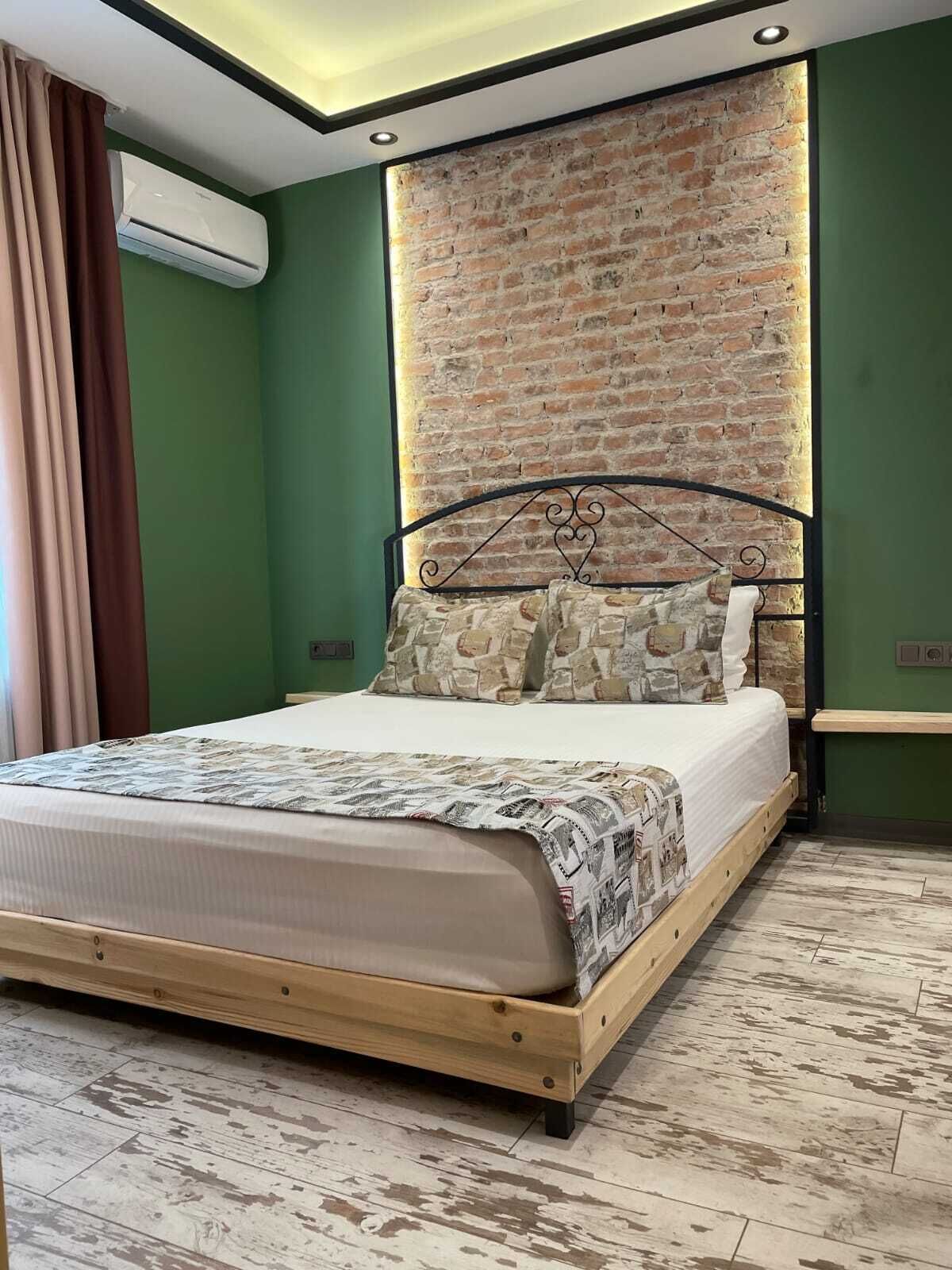 A bedroom with a brick wall, a wooden bed frame, and a green wall.
