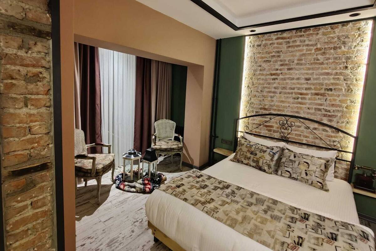 A bedroom with a brick wall, a bed with patterned bedding, a chair, and a small table with a tray.