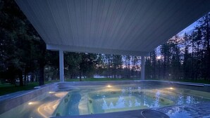 A hot tub under a covered area with a view of trees and a sunset.