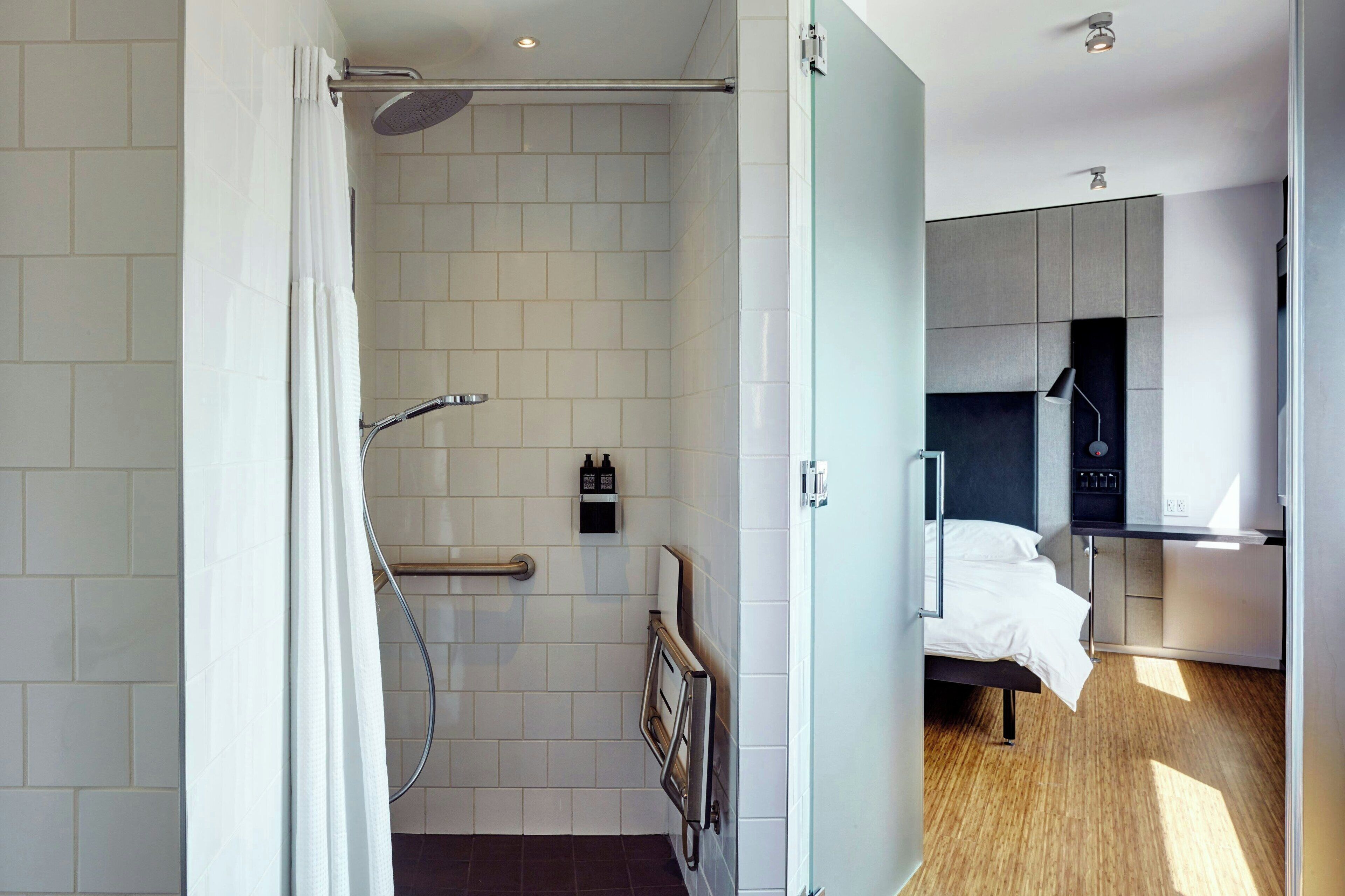 A modern bathroom with a shower, toilet, and a bed in a separate room.
