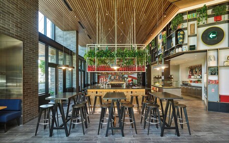 A modern cafe with high ceilings, wooden beams, and a central bar area.