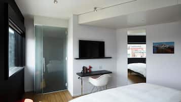 Une chambre d’hôtel moderne équipée d’un lit, d’un bureau avec une chaise, d’une télévision et d’une porte en verre donnant sur une salle de bain.