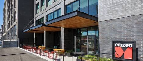 Un bâtiment moderne, avec une enseigne indiquant qu’il s’agit d’un hôtel de la chaîne Citizen, une zone de sièges en plein air et un patio couvert.