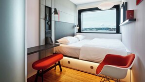 A modern bedroom with a bed, a bench, a desk, and a large window offering a city view. - citizenM Seattle Pioneer Square (Seattle)