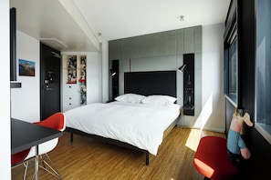 A modern bedroom with a large bed, a desk, and two red chairs.