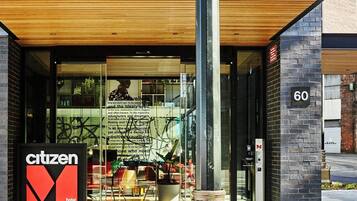 Una entrada de hotel moderna con fachada de vidrio, un alero de madera y un llamativo letrero que dice 'Citizen Hotel'.