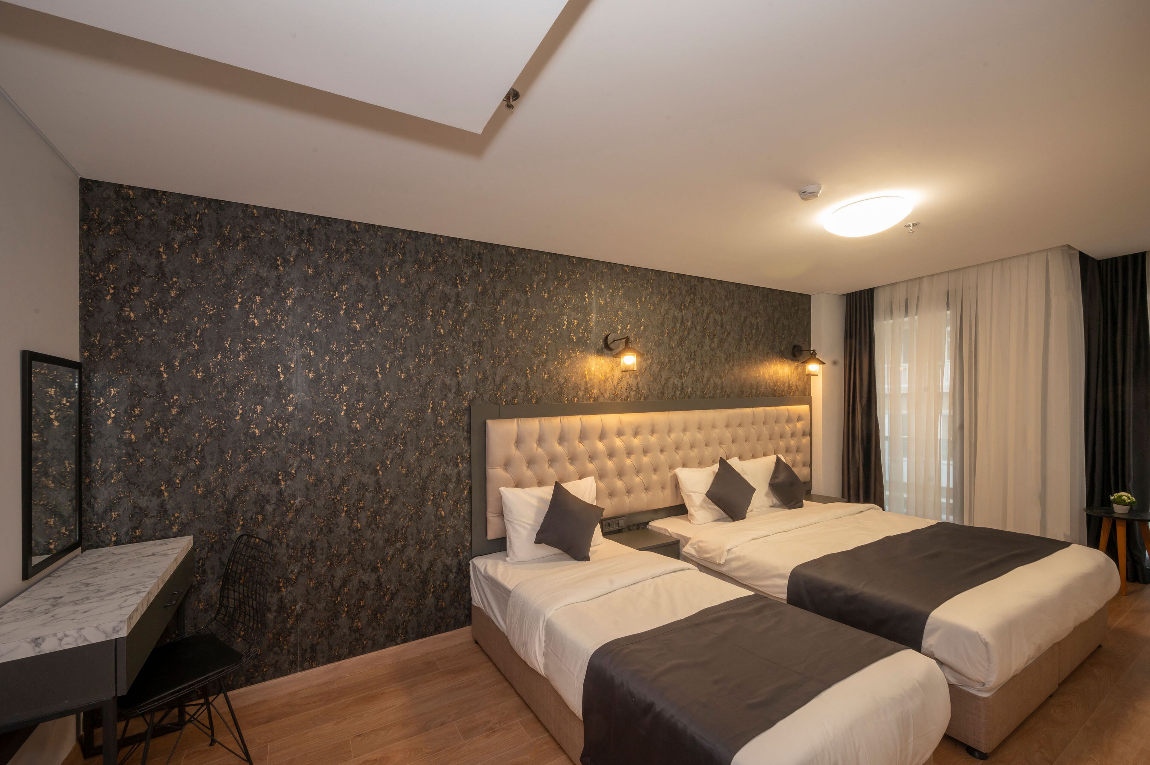 Une chambre d’hôtel avec deux lits, un bureau et une grande fenêtre avec des rideaux.