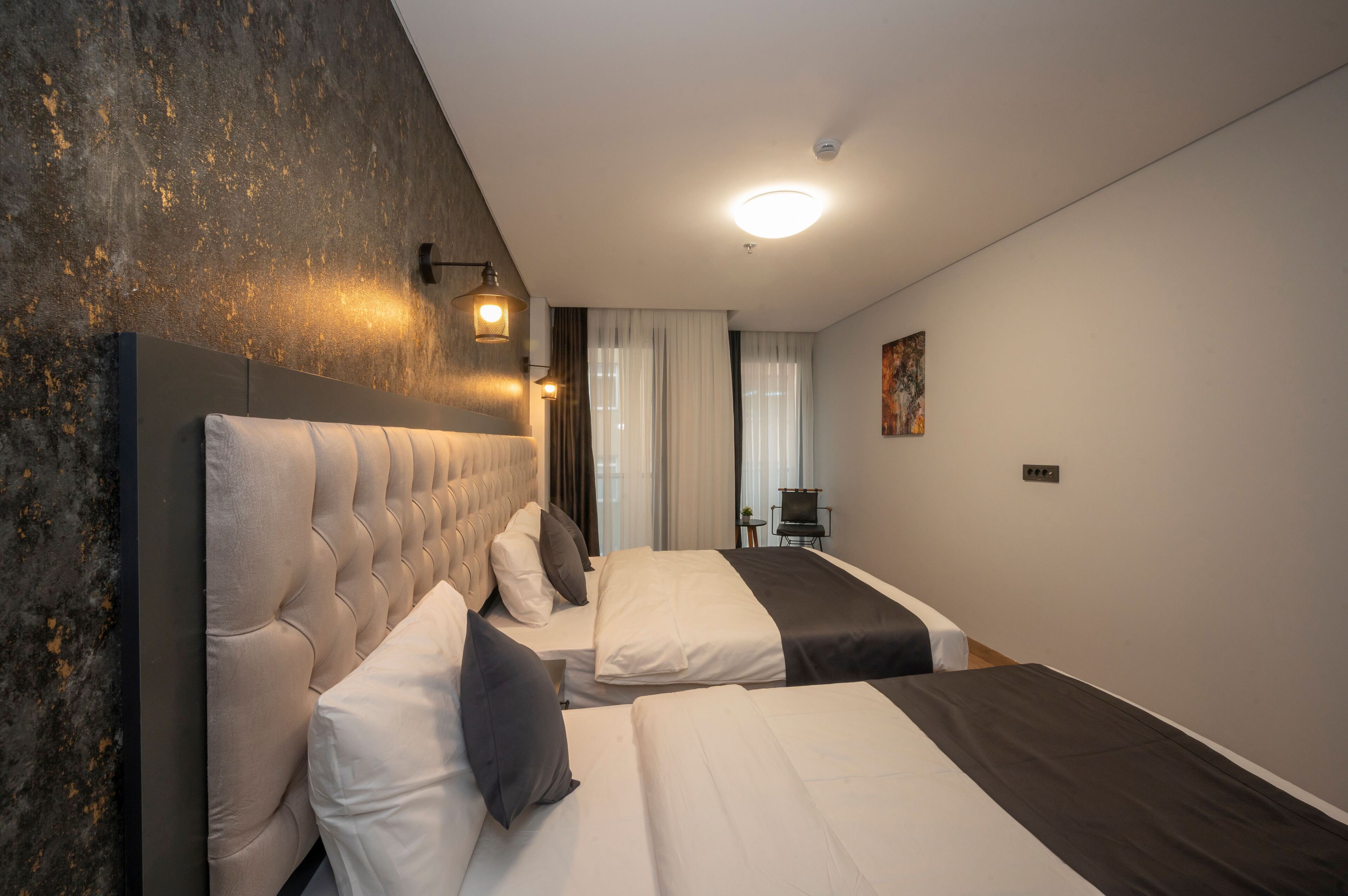 A modern hotel room with a large bed, a smaller bed, and a seating area with a chair and table.