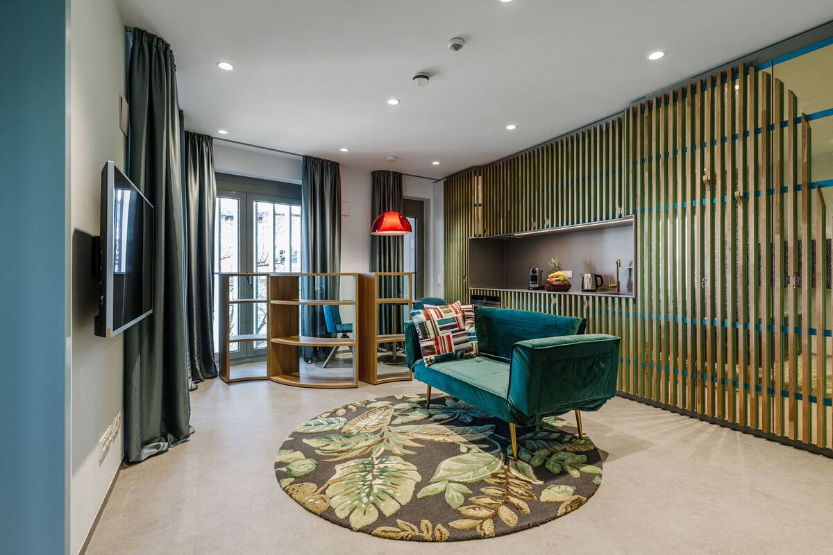 A modern living room with a teal sofa, a round rug, and a wooden bookshelf.