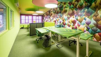 Una habitación con alfombra verde, una mesa verde y una pared colorida con un diseño de hojas.