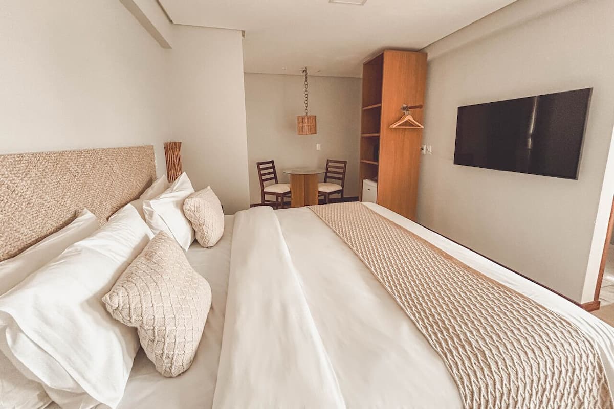 Una habitación de hotel moderna con una cama grande, un televisor montado en la pared y un comedor con sillas y una mesa.