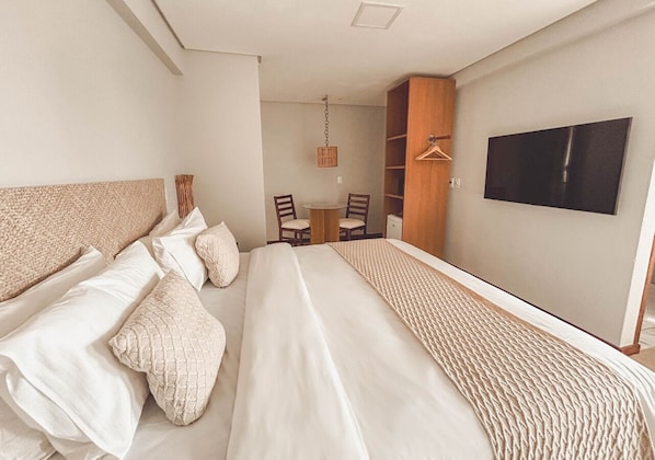 Moderni hotellihuone, jossa on suuri sänky, seinälle asennettu televisio sekä ruokailutila, jossa on tuoleja ja pöytä.