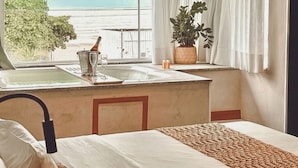A hotel room with a bed, a small kitchenette with a sink, a potted plant, and a view of the beach.