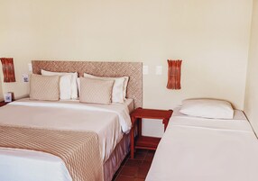 Una camera d'albergo con un letto grande, un letto più piccolo, un comodino in legno e una lampada a parete.