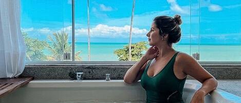 Eine Person in einer Badewanne mit Blick auf den Ozean und Palmen.