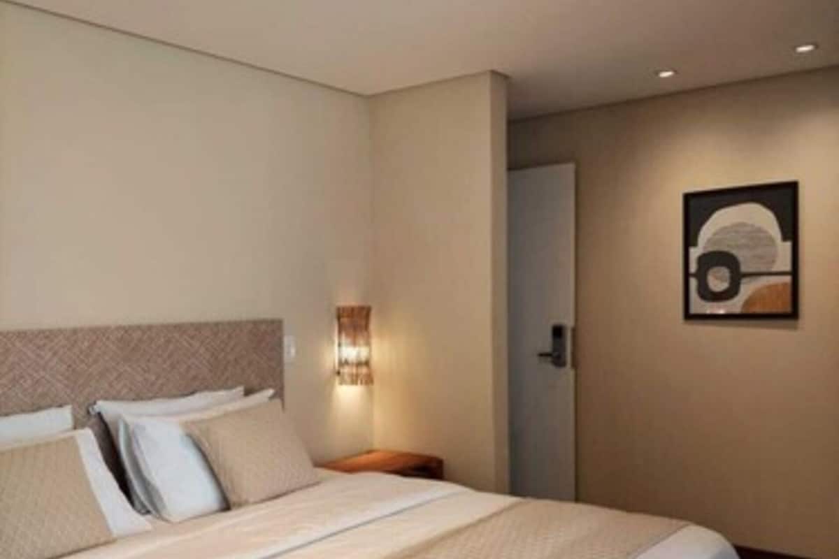 Habitación de hotel con una cama grande, una mesita de noche, una lámpara de pared y un cuadro en la pared.