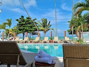 A poolside area with lounge chairs, a small table with a towel, and a view of the ocean.