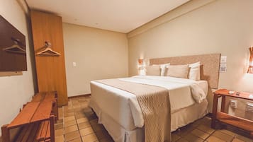 Una habitación de hotel con una cama, un banco, una percha de madera y una mesita de noche.