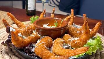A plate of breaded shrimp with a dipping sauce, a bottle of wine, and a glass of wine on a table.