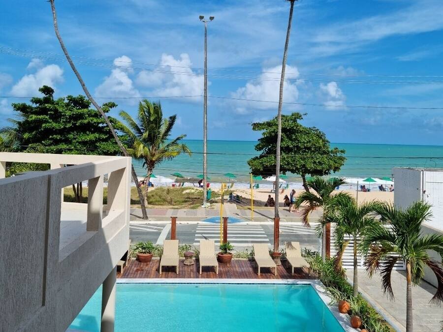 A pool area with lounge chairs, a view of the beach, and palm trees.