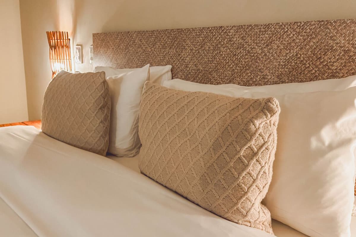 Una cama con cabecera trenzada, dos almohadas y una lámpara de noche.