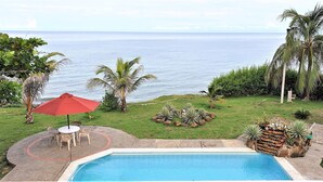 Un patio trasero con piscina, muebles de jardín y vista al océano.