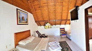 Un dormitorio con techo de madera, una cama con ropa de cama blanca, una silla con una manta a rayas y un cuadro en la pared.