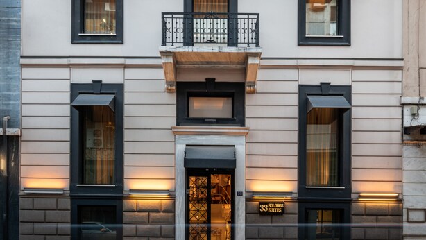 Ein Gebäude mit einer symmetrischen Fassade, großen Fenstern und einem zentralen Eingang, der eine Schilder mit der Aufschrift „33 Solanas Suites“ zeigt.