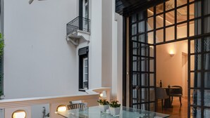 Ein Tisch mit Glasplatte, vier Stühle, ein kleiner Topfpflanze und ein Fenster mit Balkon.