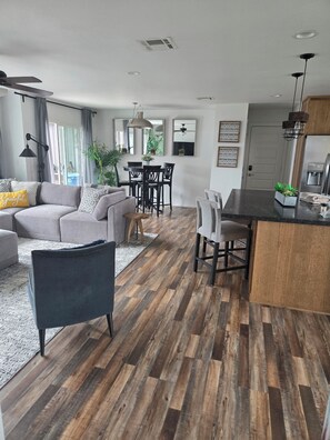 A modern living room with a sofa, chairs, a dining table, and a kitchen area with a refrigerator and sink.