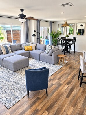 A modern living room with a sectional sofa, a blue armchair, a dining area with a table and chairs, and a ceiling fan. - 3 Bedroom, 2 Bath, Clean, Bright, Modern Space, in a Quite, Modest Neighborhood  (Grants Pass)