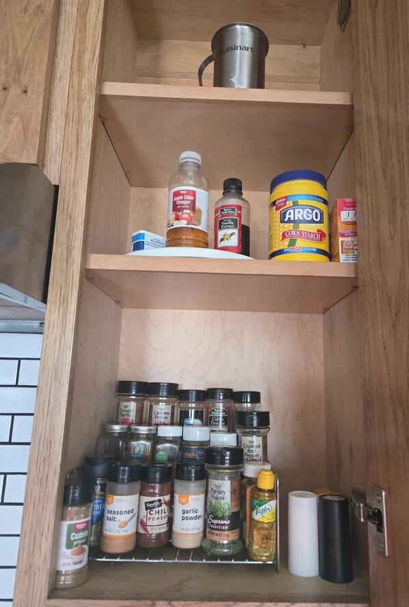 Un meuble de cuisine contenant divers aliments et récipients, notamment des épices, des sauces et un bocal de fécule de maïs.