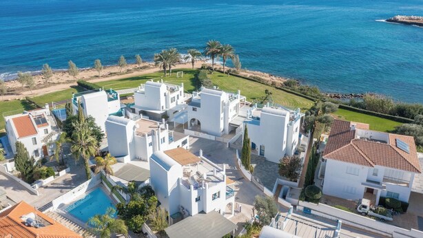 A coastal residential area with white buildings, a swimming pool, and a view of the sea.
