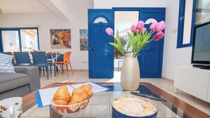 A living room with a glass coffee table holding croissants, a bowl of croissants, a vase with tulips, and a container of biscuits.