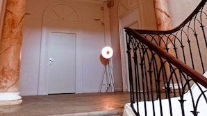 Uma escadaria com colunas de mármore, um corrimão de metal preto e uma porta branca no topo.