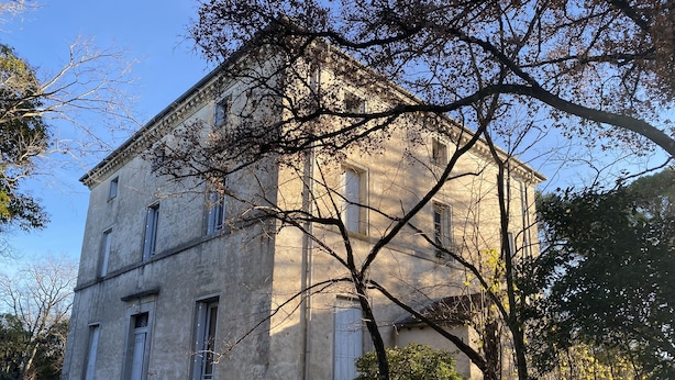 Um grande edifício histórico de pedra, com fachada simétrica, várias janelas e uma entrada central com degraus.