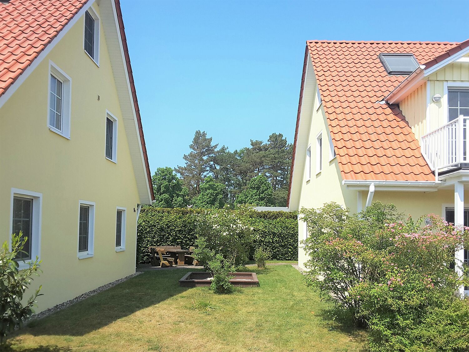 A courtyard with two yellow buildings, a wooden table, and a small garden area.